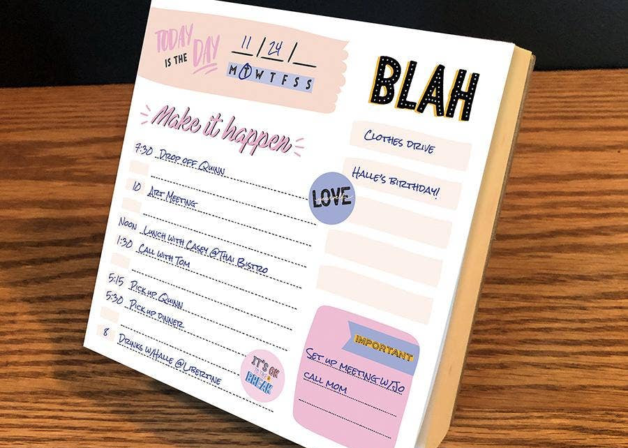 A colorful desk planner page on a wooden surface displays a daily schedule with handwritten tasks. Words like "Blah" and "Love" add a playful tone.