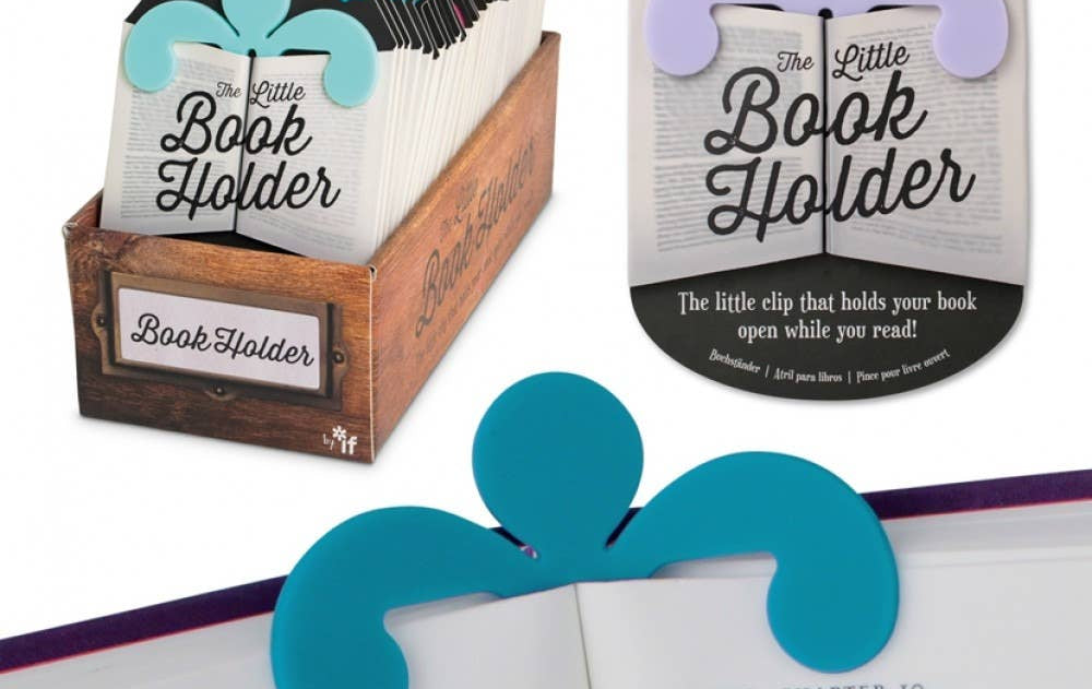 A colorful book holder clip is shown in use, holding a book open. The package has decorative designs and text reading "The Little Book Holder." Display box is visible.