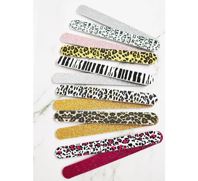 An assortment of ten glittery and patterned emery board nail files fanned out on a white marble background, featuring zebra stripes, cheetah print, and hot pink leopard print.