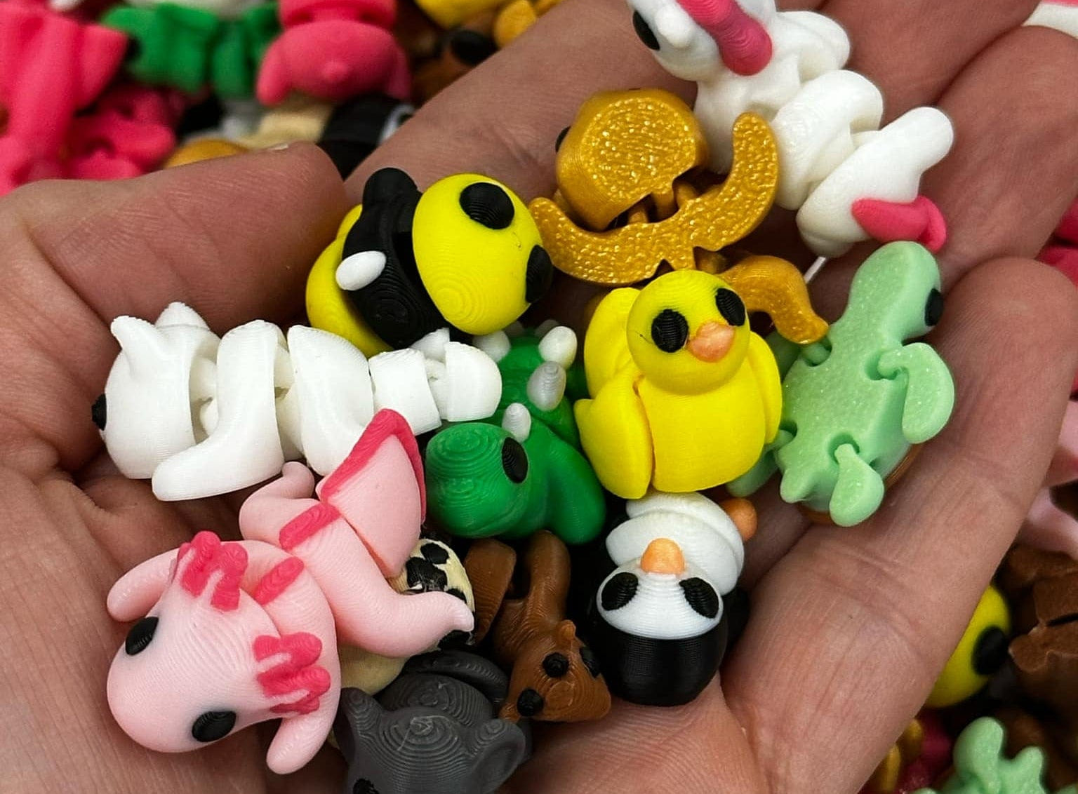 A hand holding several small, colorful toy fidget pets, including representations of a pink dog, a yellow duck, and others with less clear designs.