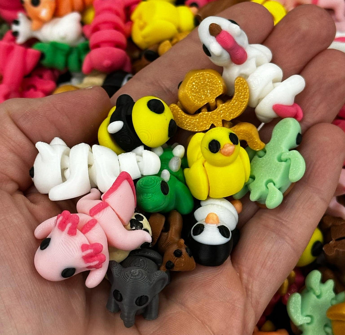 A hand holding several small, colorful toy fidget pets, including representations of a pink dog, a yellow duck, and others with less clear designs.
