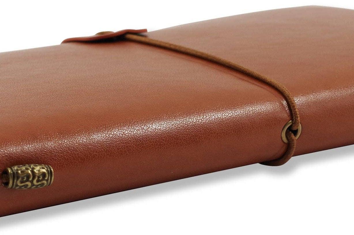 Brown leather notebook with a wraparound cord, closed, resting on a white surface. Pages slightly visible, conveying a vintage, elegant feel.