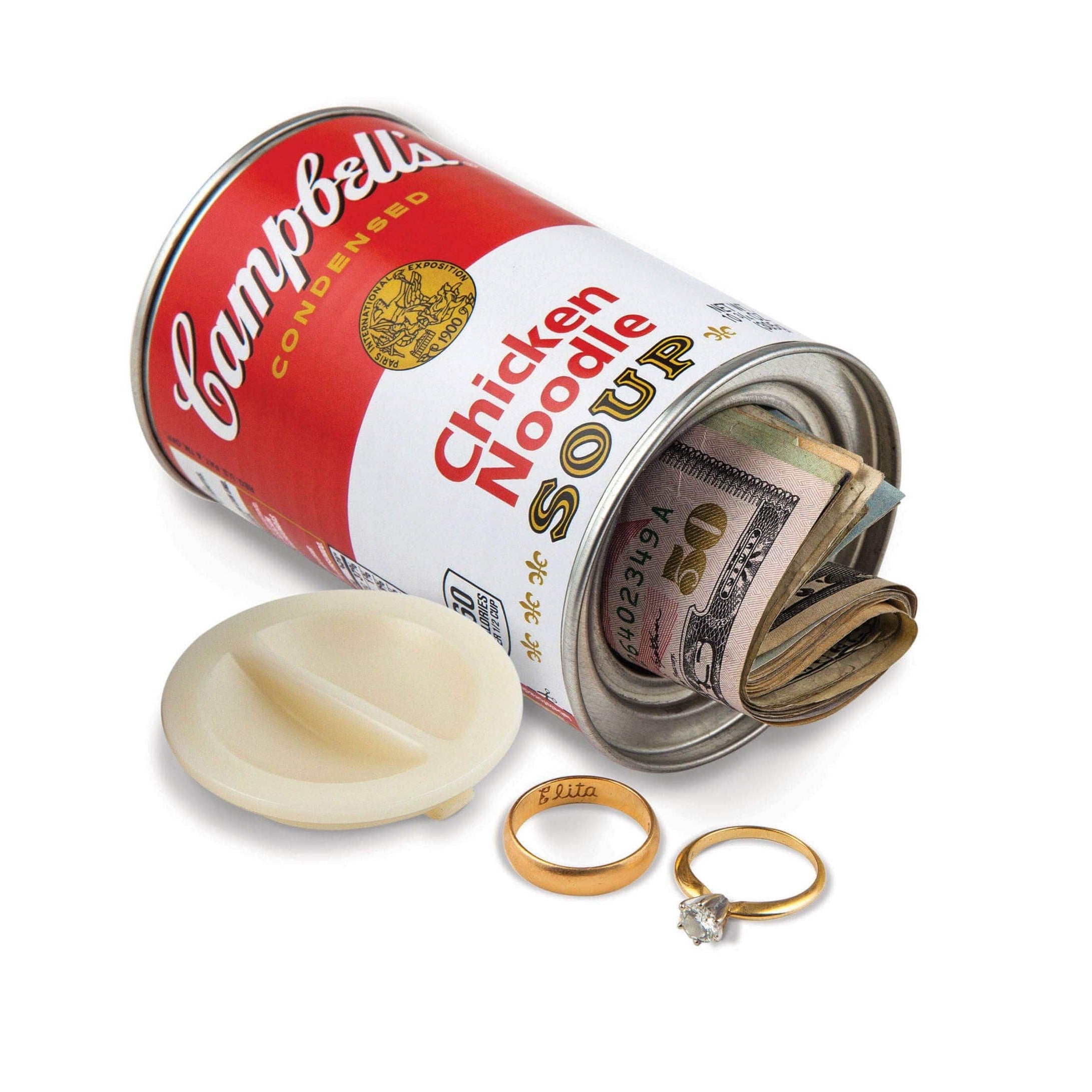 A Campbell's Chicken Noodle Soup can, with its lid removed, reveals rolled U.S. dollar bills inside. Two rings are placed nearby, evoking a sense of hidden treasure.