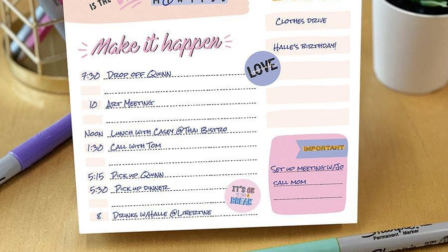 A colorful daily planner on a wooden desk, titled "Make it happen," lists various tasks with times. Nearby are a pen holder, marker, and potted plant.