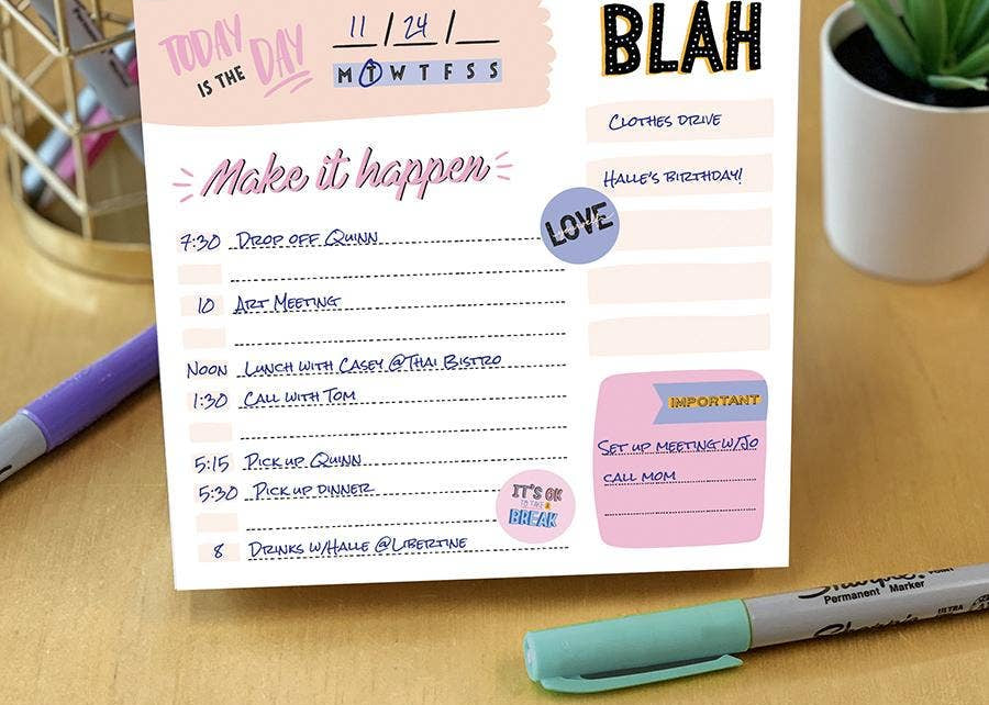 A colorful daily planner on a wooden desk, titled "Make it happen," lists various tasks with times. Nearby are a pen holder, marker, and potted plant.