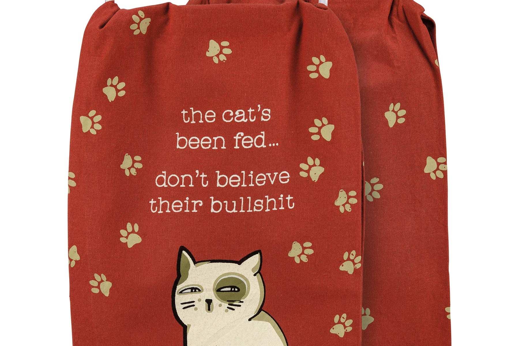 A whimsical kitchen towel with a red background, featuring cat paw prints. A cartoon cat sits below the humorous text: "the cat's been fed... don't believe their bullshit."