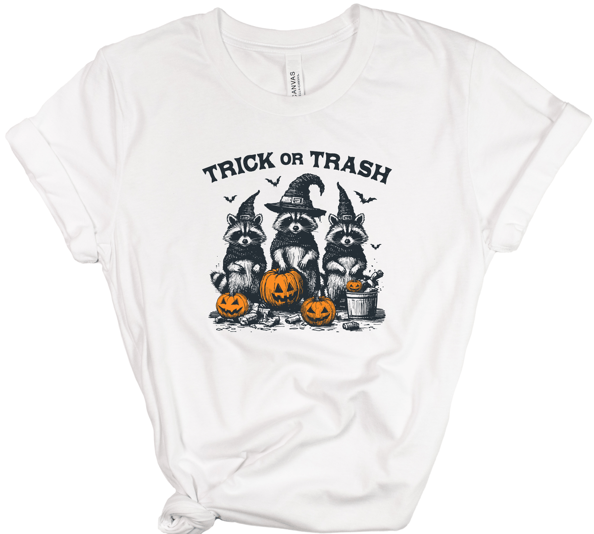 A white short-sleeve crewneck t-shirt with a graphic of three raccoons dressed as witches holding pumpkins, with the text 'TRICK OR TRASH' above them.