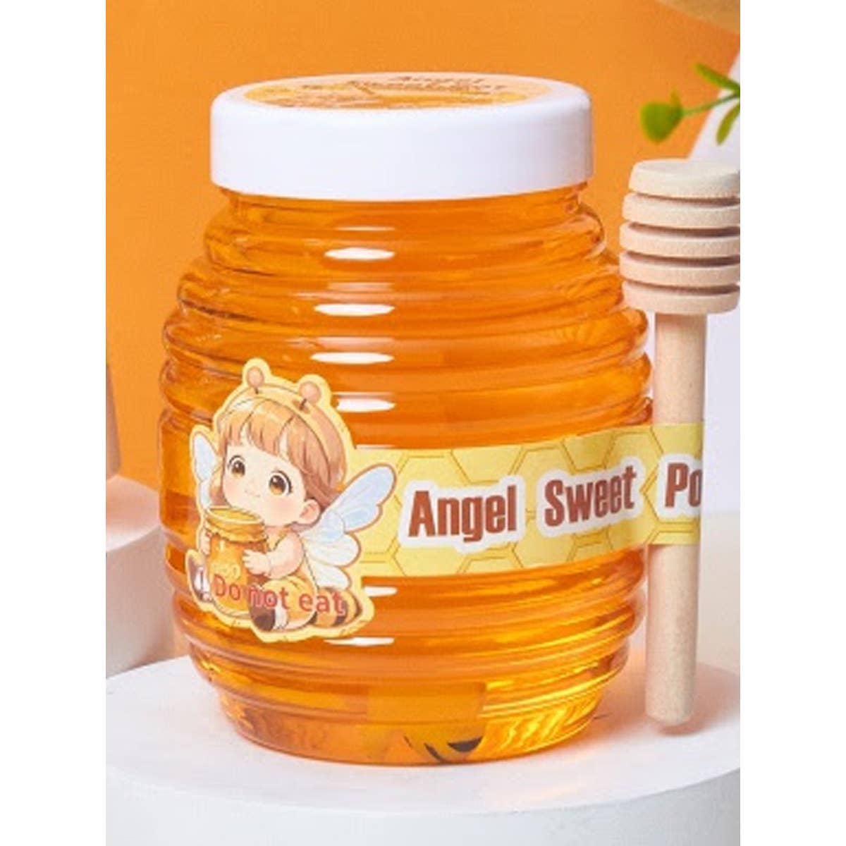 Close-up of an Angel Sweet Pot bubble slime jar shaped like a honey pot, filled with translucent amber-colored slime, featuring a bee-themed label with a cartoon child and “Do not eat” text, alongside a wooden honey dipper.