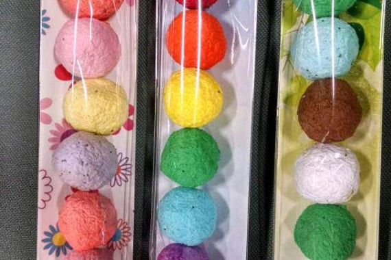Three plastic-wrapped strings of colorful textured balls are displayed vertically. Each string has pastel and bright hues on floral and abstract backings.