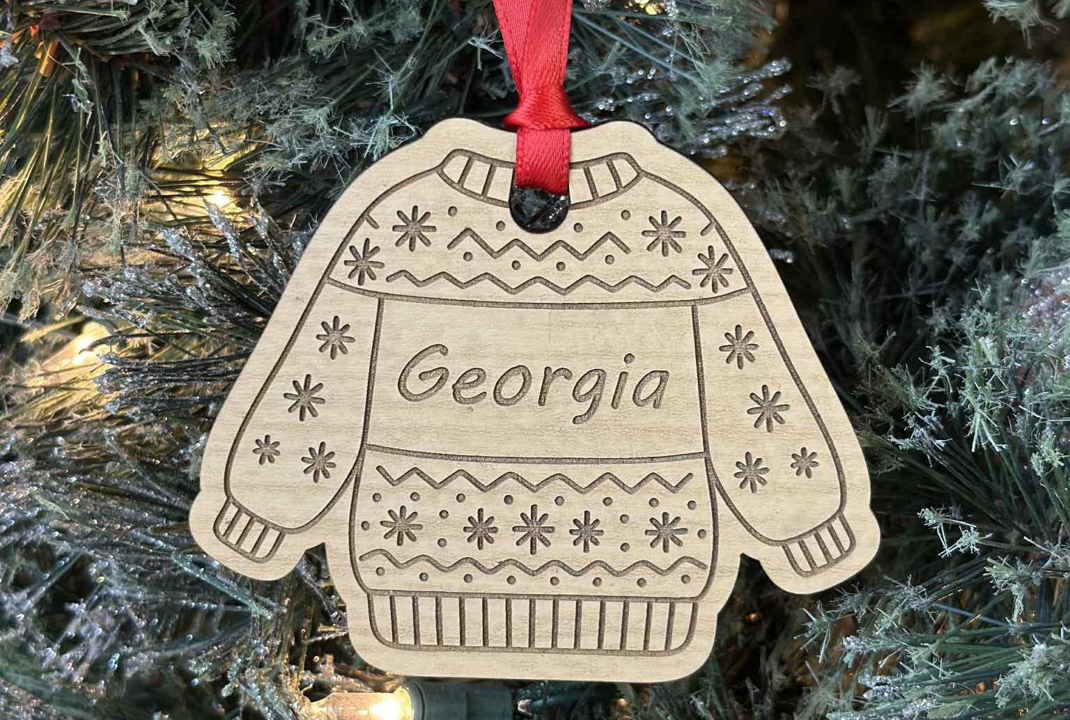 Decorative ornament shaped like a sweater with 'Georgia' on it, hanging on a Christmas tree.