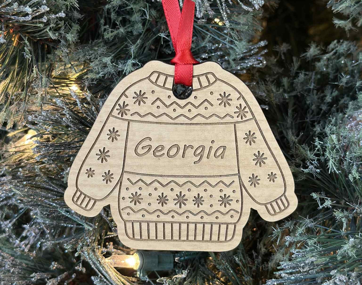Decorative ornament shaped like a sweater with 'Georgia' on it, hanging on a Christmas tree.