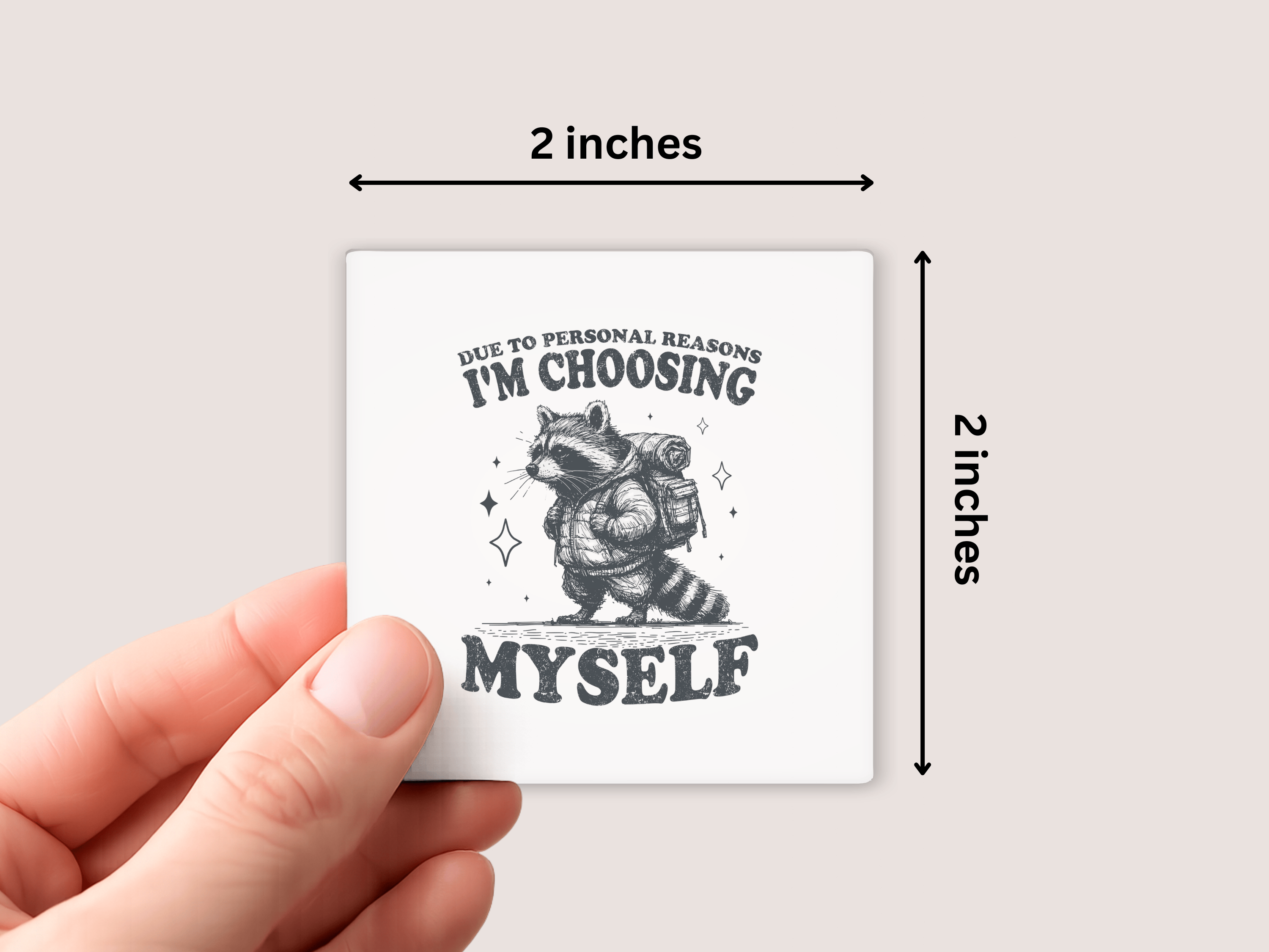white square magnet with a raccoon illustration and text held by a hand, with dimensions indicated.