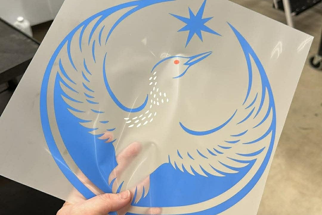 Hand holding a DTF print of the rebel loon design with blue and white colors in an indoor setting.
