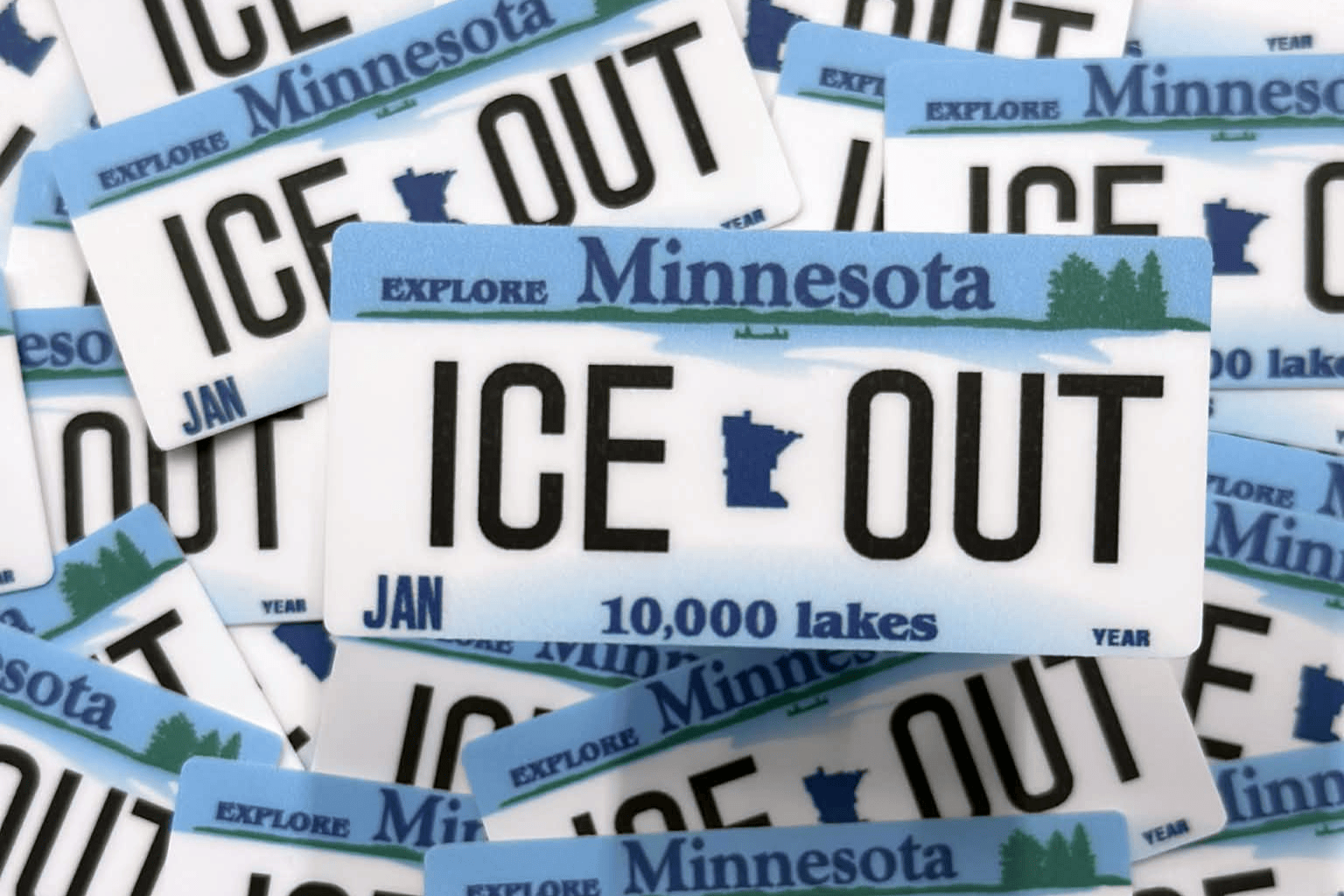 Stack of 'ICE OUT' Minnesota license plates with text about lakes.