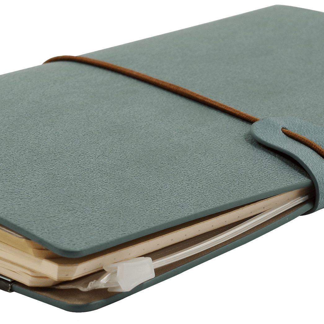 A closed gray-blue leather journal with a brown elastic strap, filled with slightly worn pages, rests on a transparent background. It conveys a vintage, well-used feel.