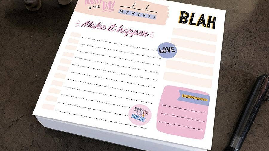A colorful notepad on a table with sections labeled "Today is the day," and "Make it happen." Nearby is a pen and decorative elephant figurine.