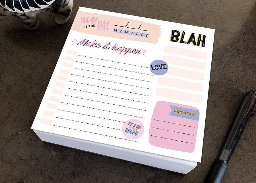 A colorful notepad on a table with sections labeled "Today is the day," and "Make it happen." Nearby is a pen and decorative elephant figurine.