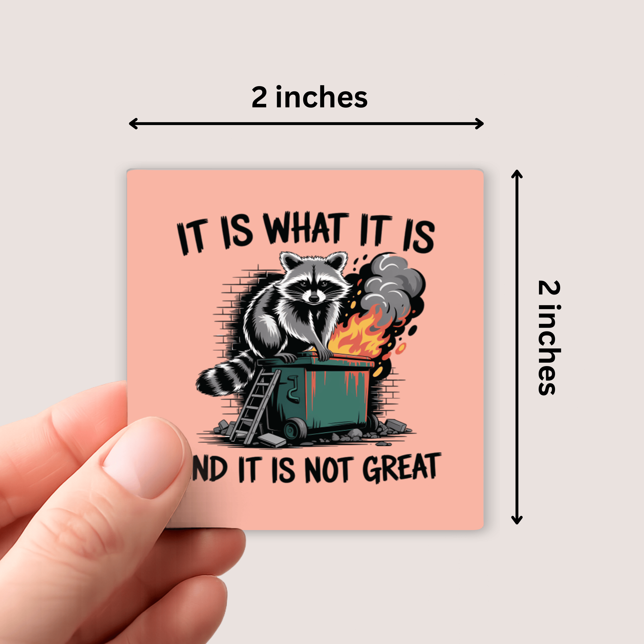 Small square card with a raccoon graphic and text, held by a hand against a light gray background.