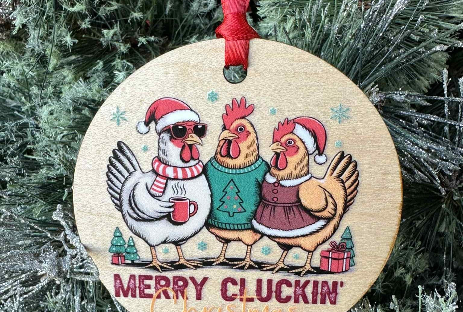 Wooden Christmas ornament with cartoon chickens wearing Santa hats and scarves, surrounded by festive decorations on a tree.