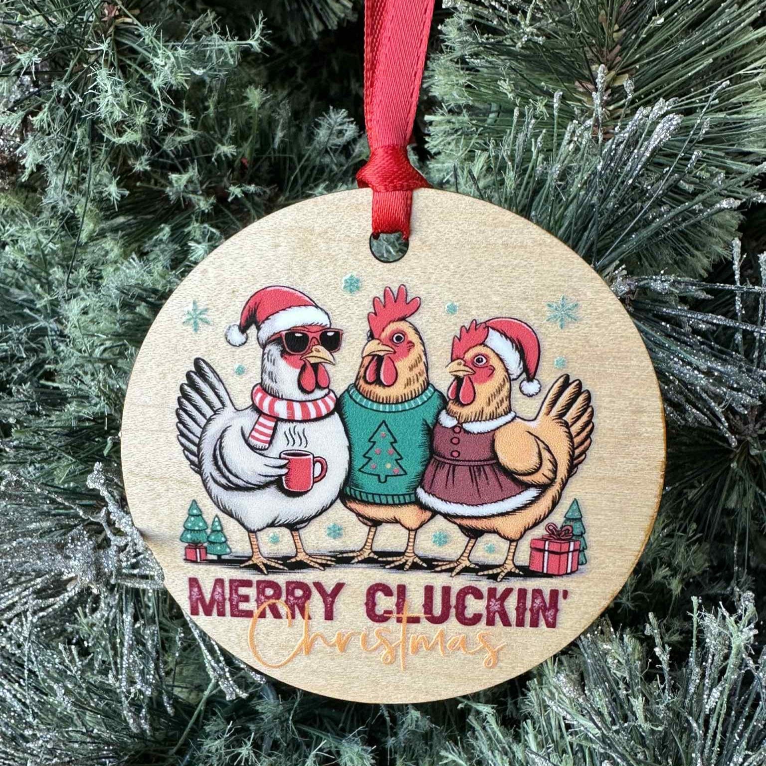 Wooden Christmas ornament with cartoon chickens wearing Santa hats and scarves, surrounded by festive decorations on a tree.