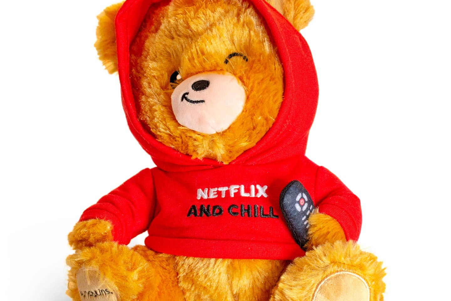 Brown teddy bear wearing a red sweatshirt with the hood up, ears sticking out the top. The bear is holding a remote and sporting a smirk. The sweatshirt features black and white embroidered text that reads 'Netflix & Chill.'