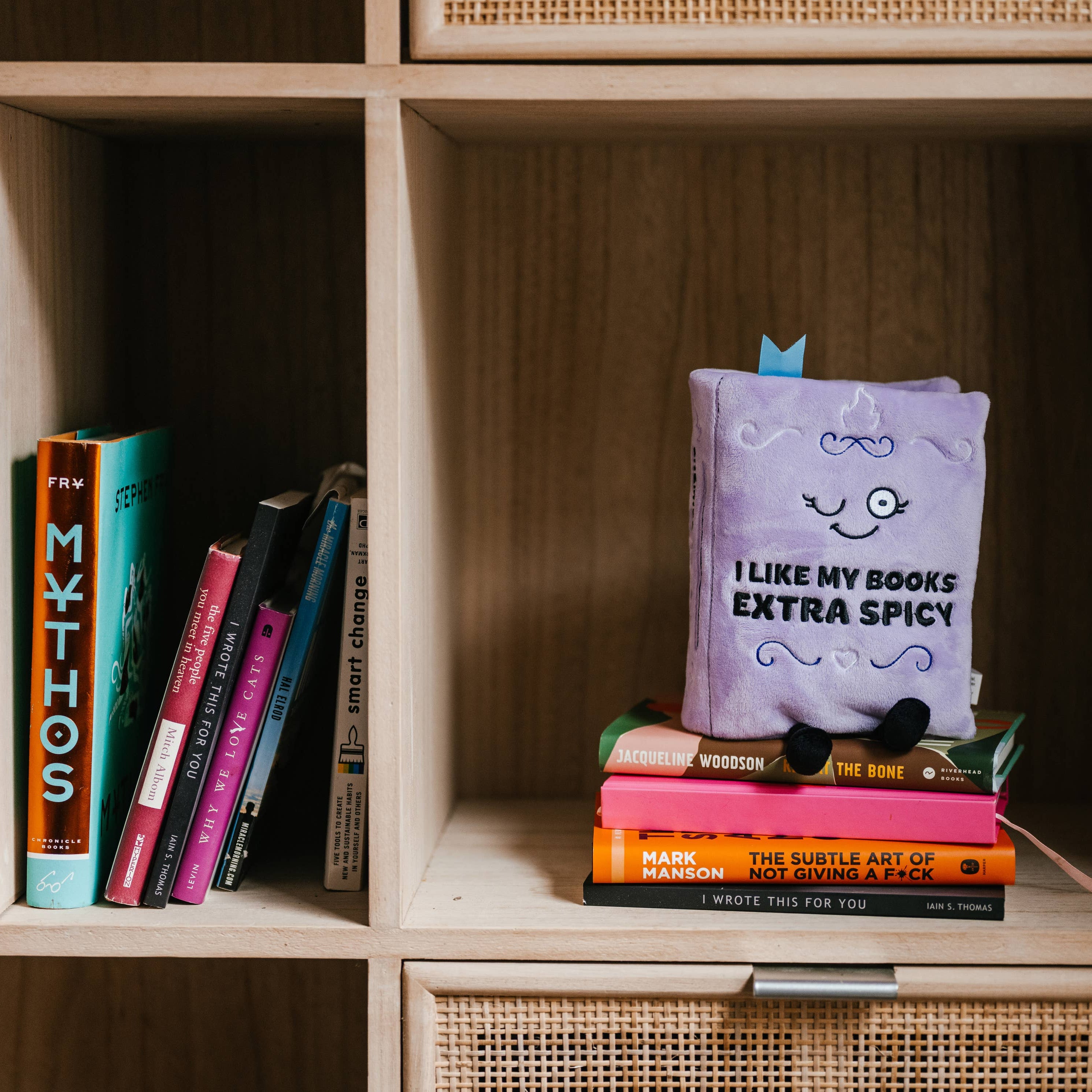 Stack of books with a purple book titled 'I Like My Books Extra Spicy' on a wooden shelf.