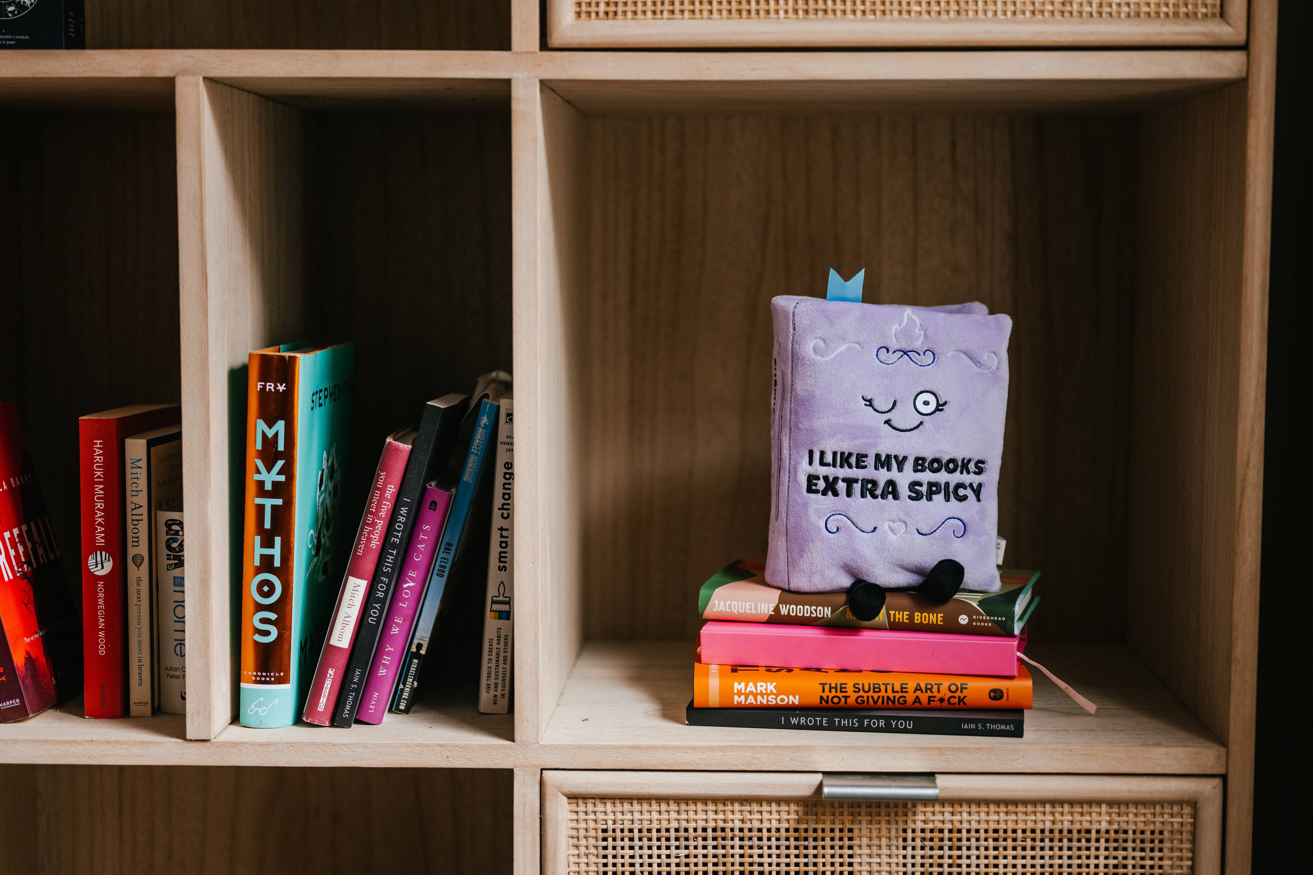 Stack of books with a purple book titled 'I Like My Books Extra Spicy' on a wooden shelf.