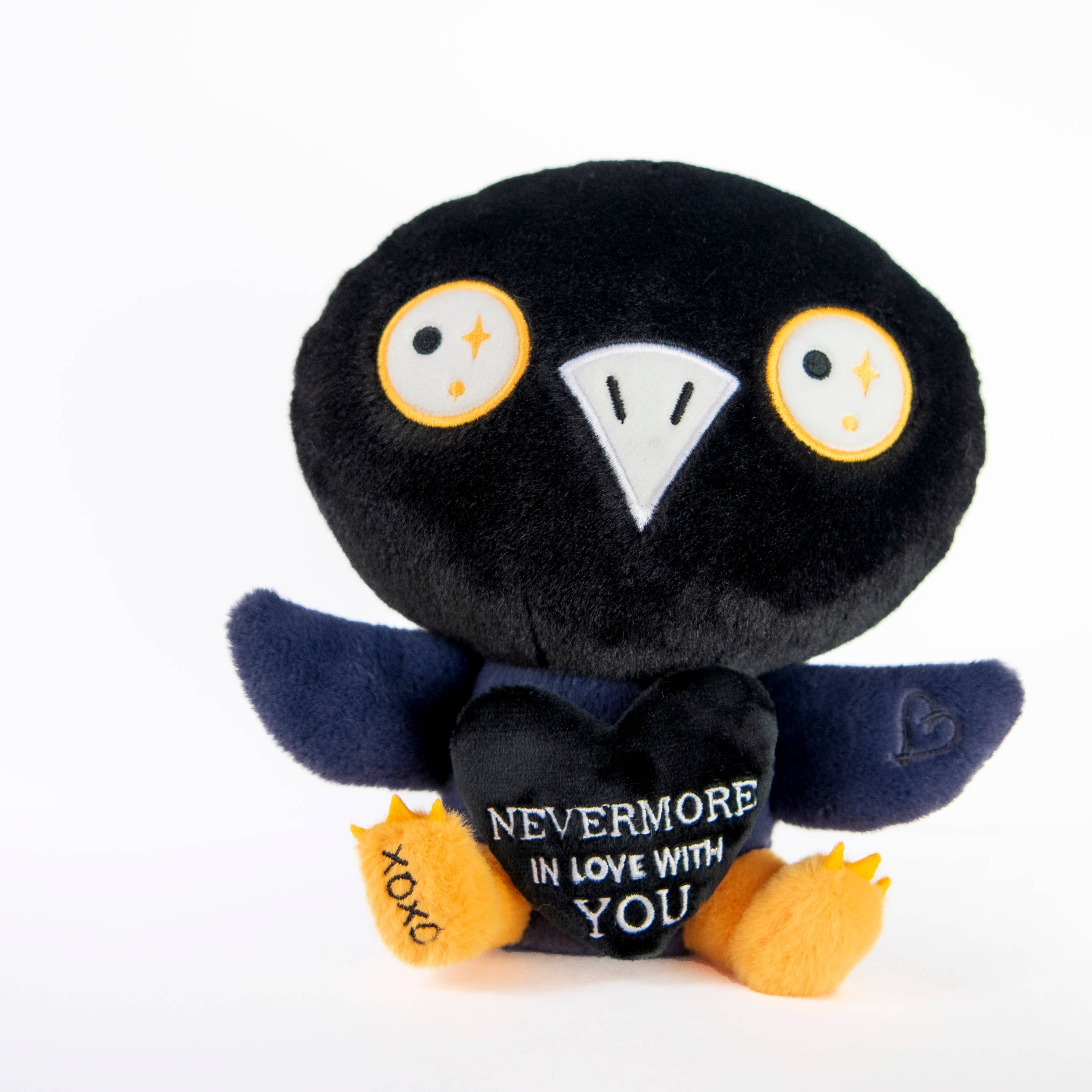 A black and blue raven plushie with a white beak and white and yellow eyes. Its wings are holding a black heart with the white text "Nevermore in love with you." The raven has yellow legs with a black "xoxo" on the right foot.