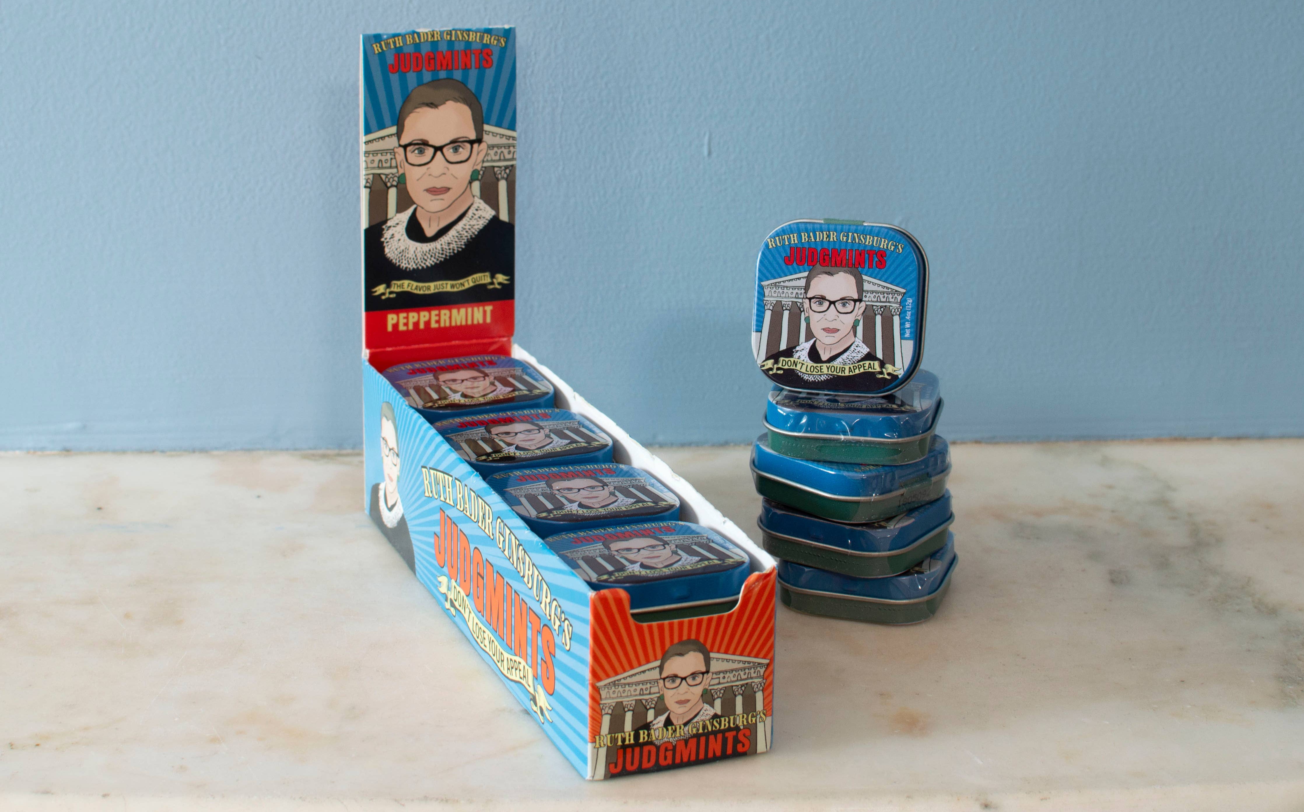 A box of peppermint mints branded as "Judgemints" with a caricature of Ruth Bader Ginsburg on the packaging, displayed against a blue background.