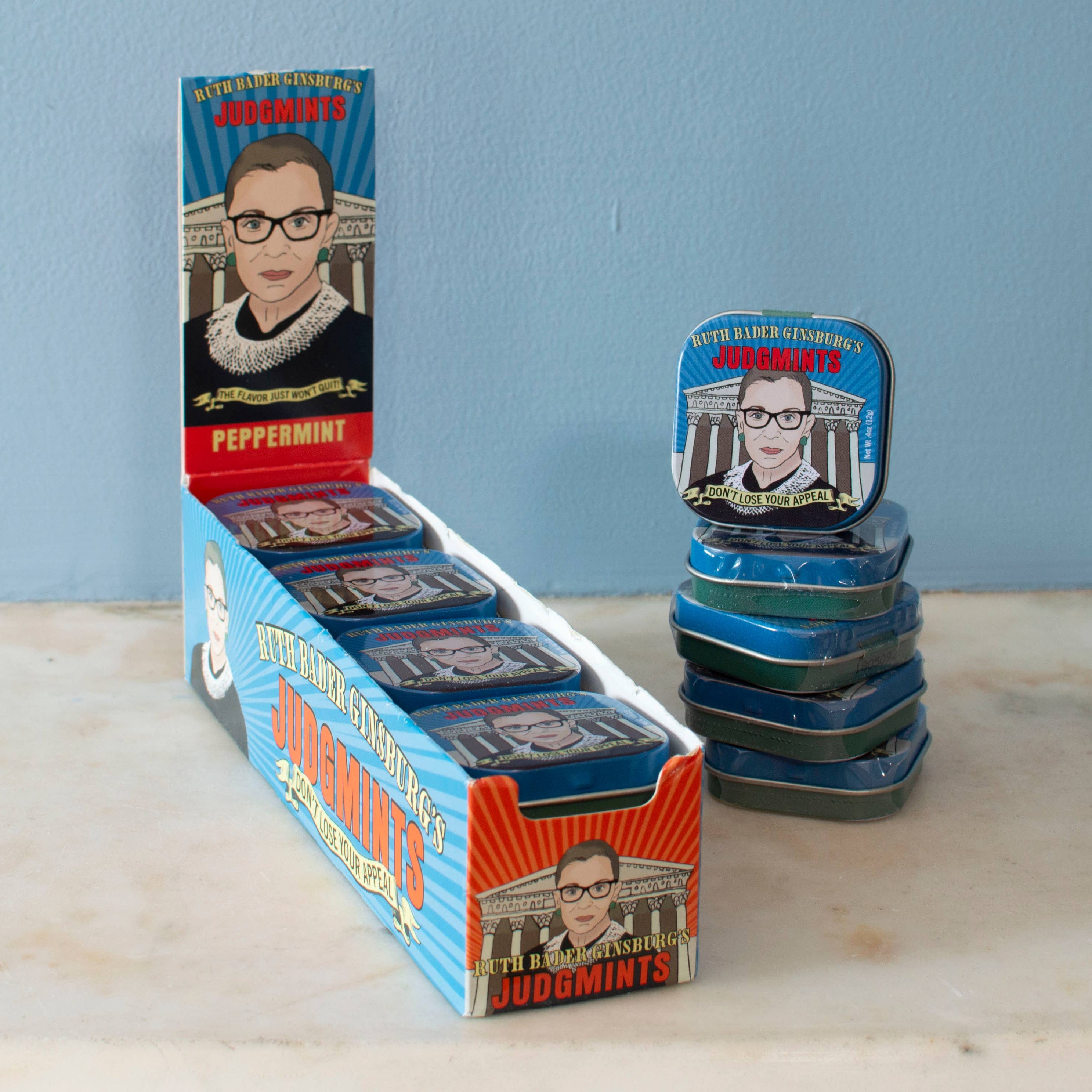 A box of peppermint mints branded as "Judgemints" with a caricature of Ruth Bader Ginsburg on the packaging, displayed against a blue background.