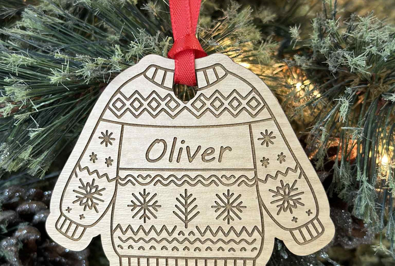 Wooden ornament shaped like a sweater with 'Oliver' on it, hanging on a Christmas tree.