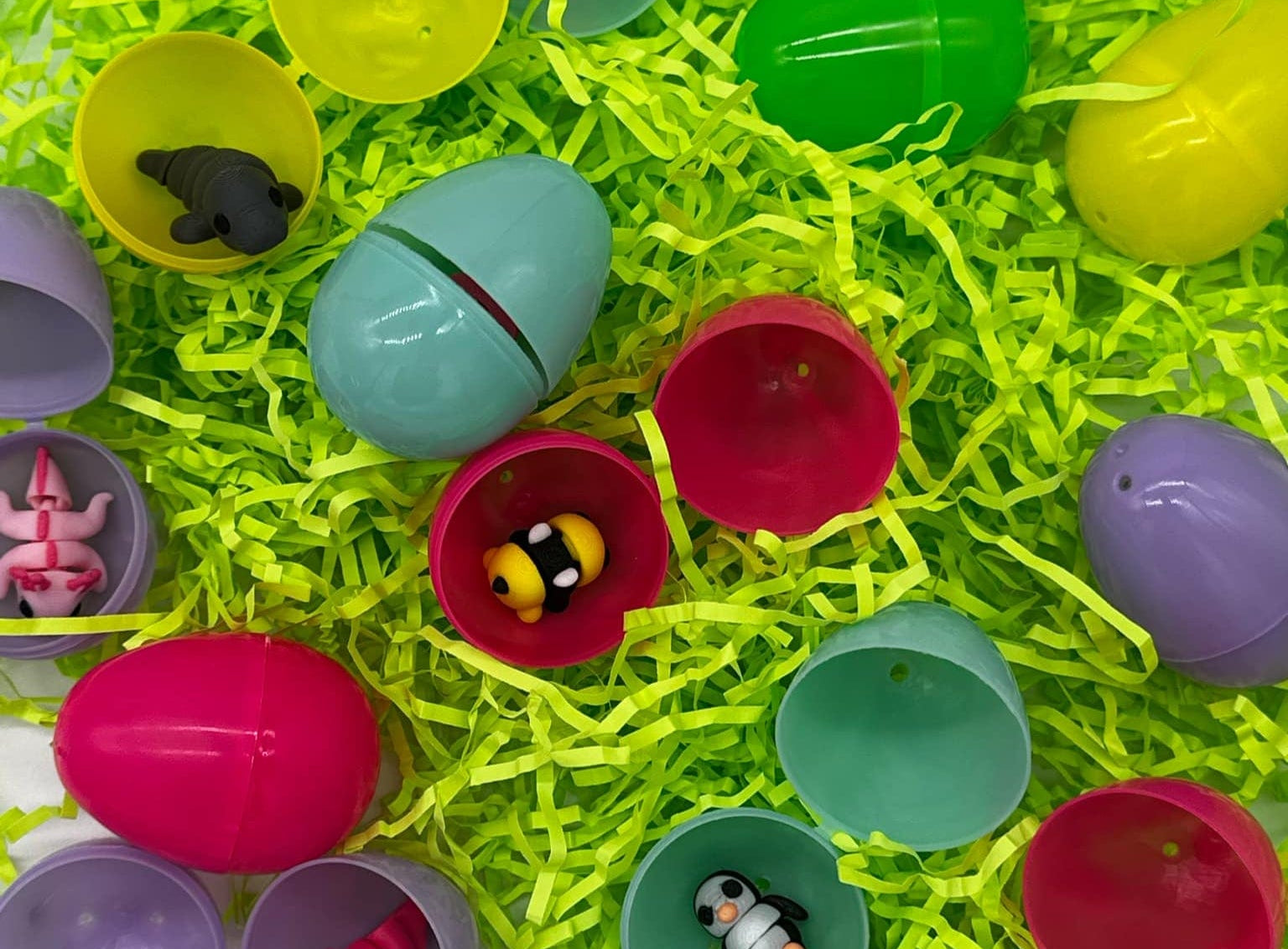 Assorted colorful plastic Easter eggs with various small toys inside, placed on green decorative grass.