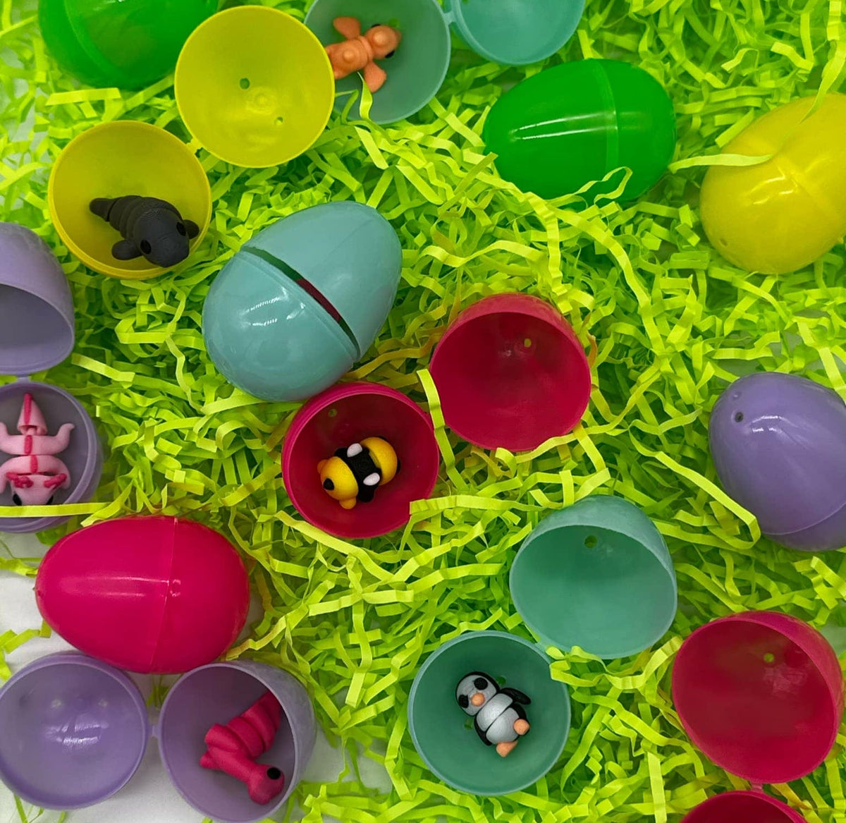 Assorted colorful plastic Easter eggs with various small toys inside, placed on green decorative grass.