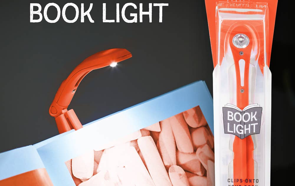 A small, orange book light is clipped to an open book, illuminating the pages. Packaging on the right showcases "The Really Tiny Book Light" branding.