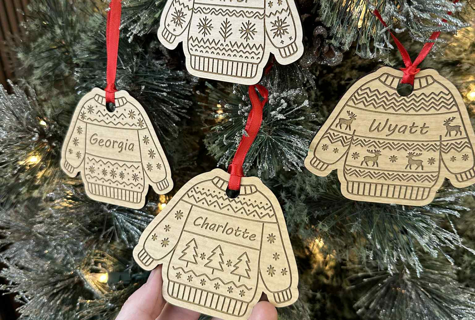 Decorative Christmas ornaments shaped like sweaters and mittens with names on a Christmas tree.