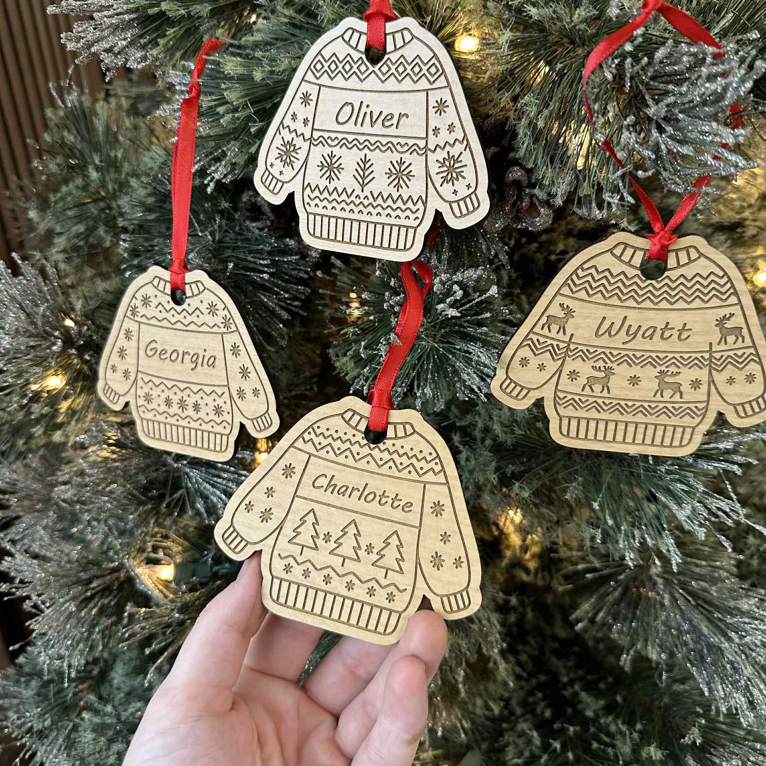 Decorative Christmas ornaments shaped like sweaters and mittens with names on a Christmas tree.