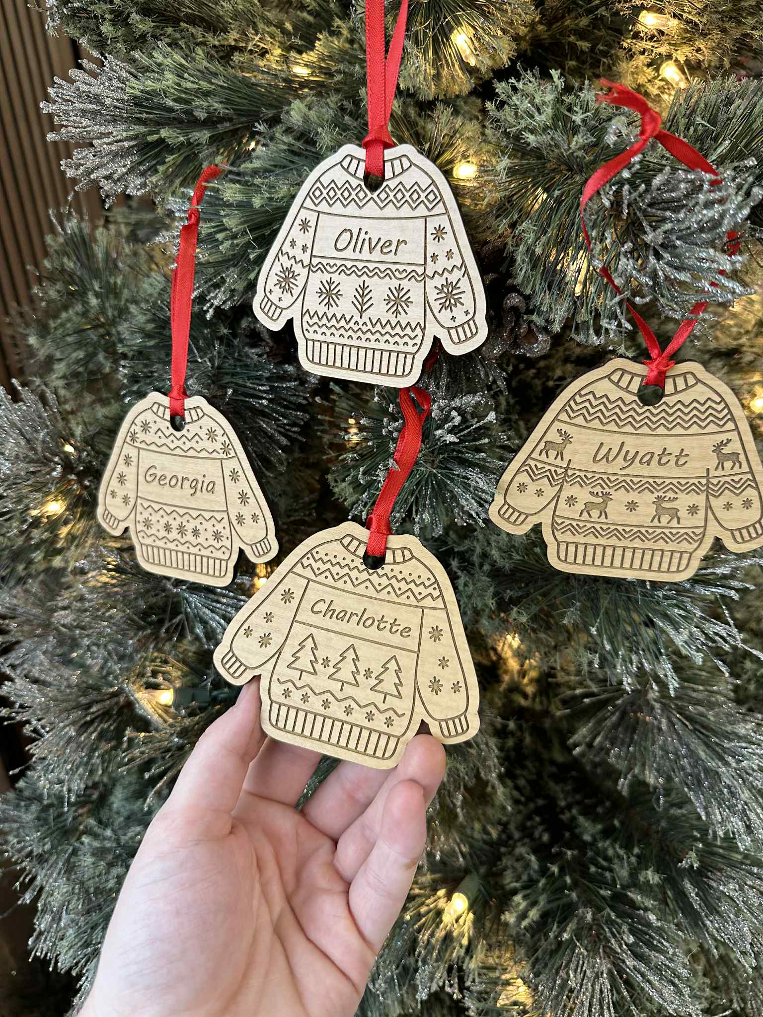 Decorative Christmas ornaments shaped like sweaters and mittens with names on a Christmas tree.