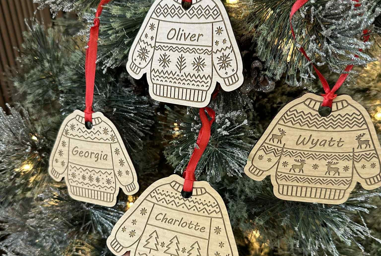 Decorative Christmas ornaments shaped like sweaters and mittens with names on a tree.