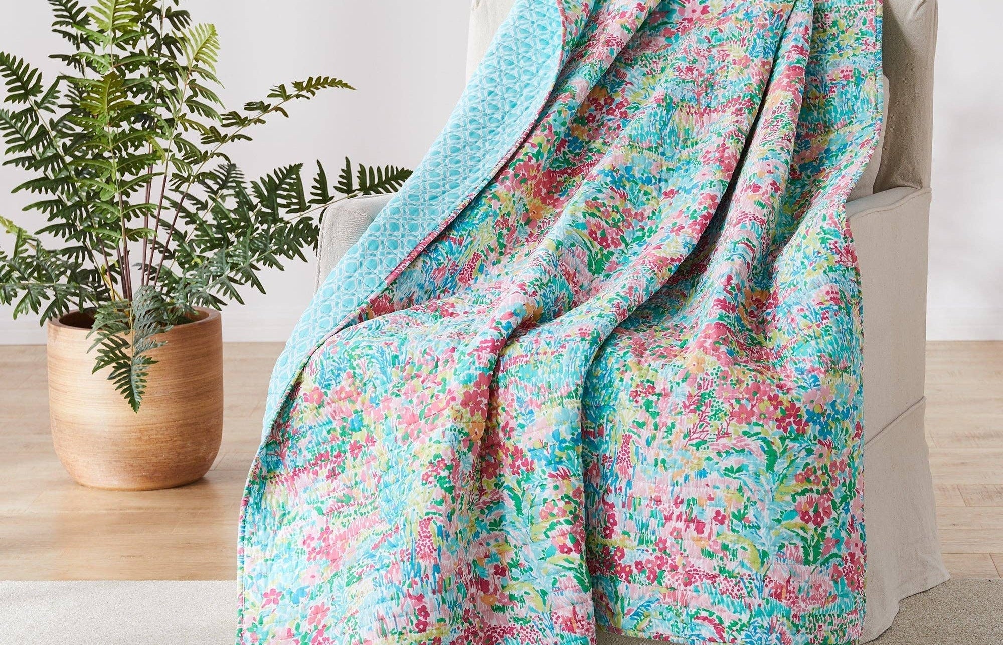 Floral patterned blanket draped over a chair next to a potted plant on a wooden floor.