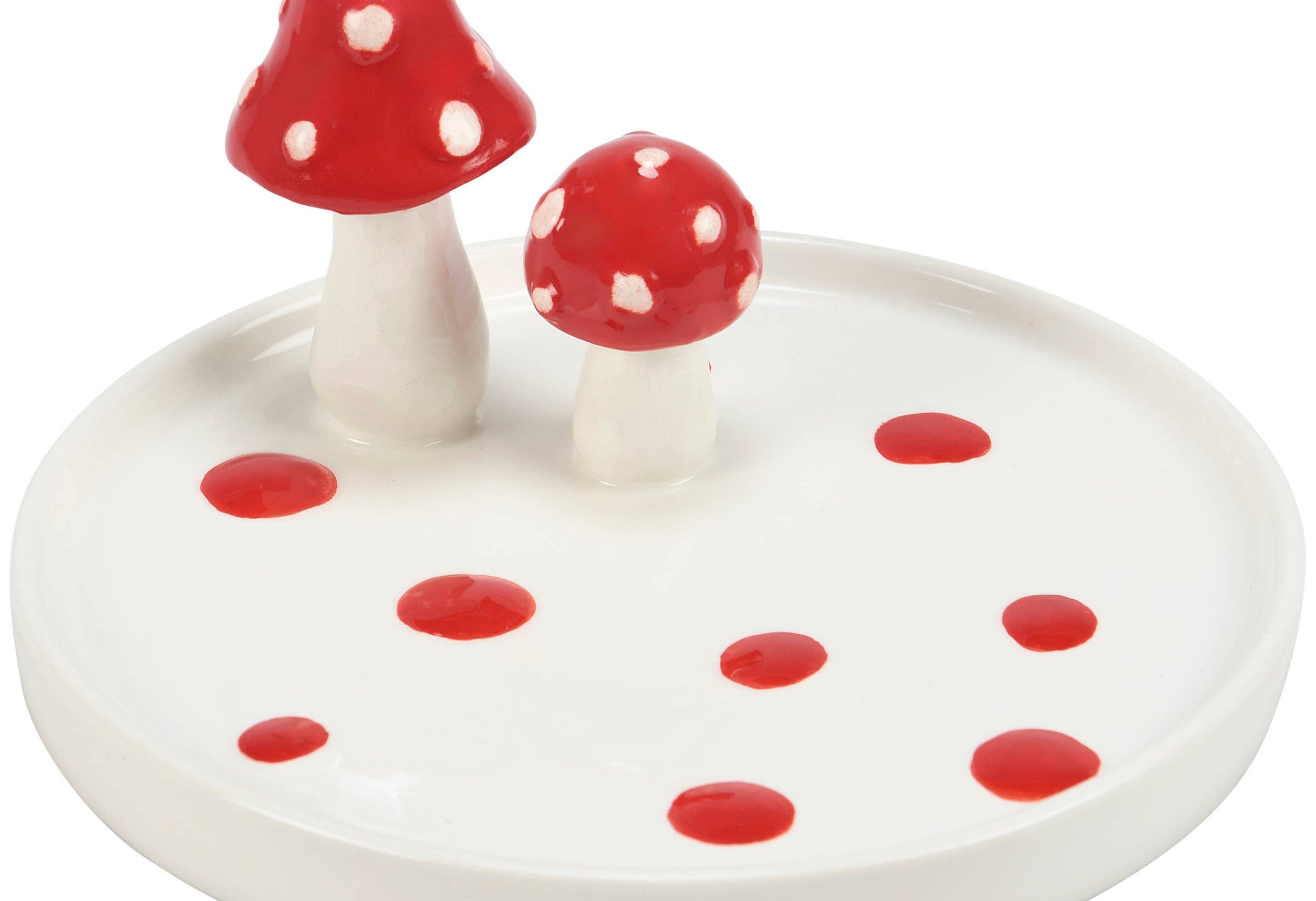 Ceramic plate featuring two red and white spotted mushroom figurines. The white plate is dotted with red spots, conveying a whimsical, decorative tone.