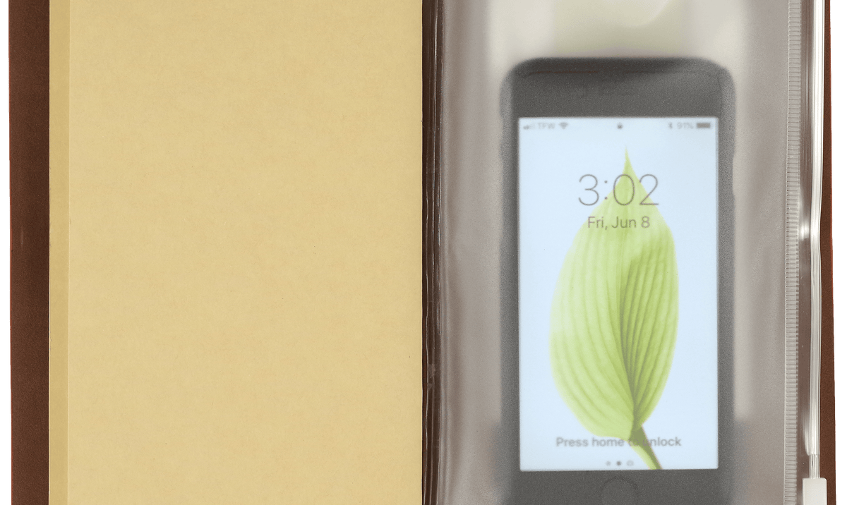 Open notebook with a beige page on the left and a smartphone inside a clear plastic sleeve on the right. The phone displays a leaf on its lock screen.