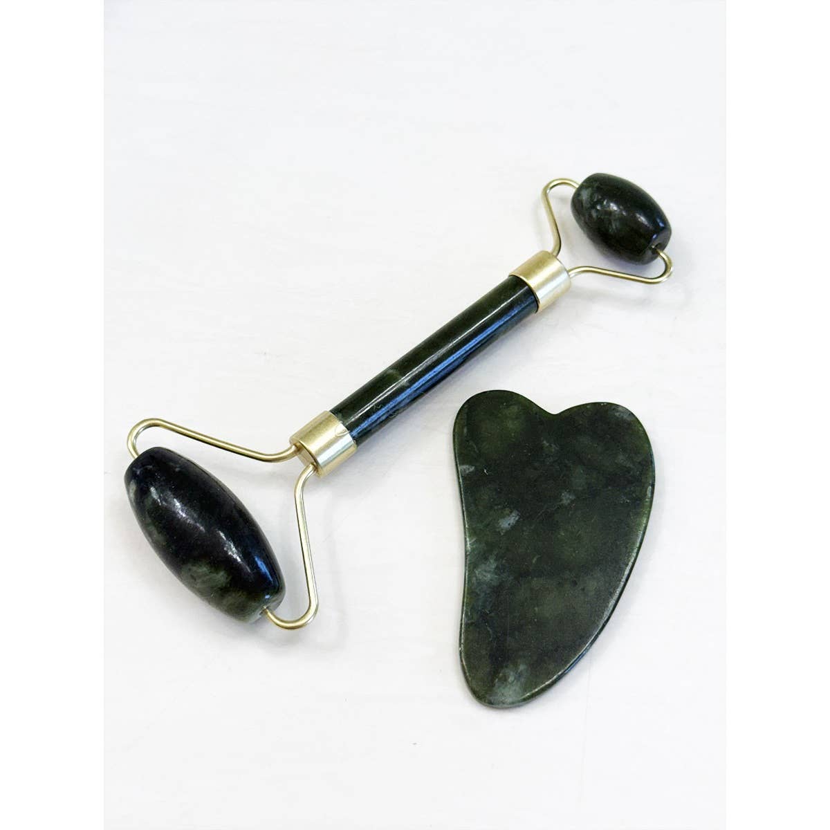 A jade roller and gua sha tool on a white background. The roller has two dark green stone ends with a gold handle, while the flat gua sha is heart-shaped.
