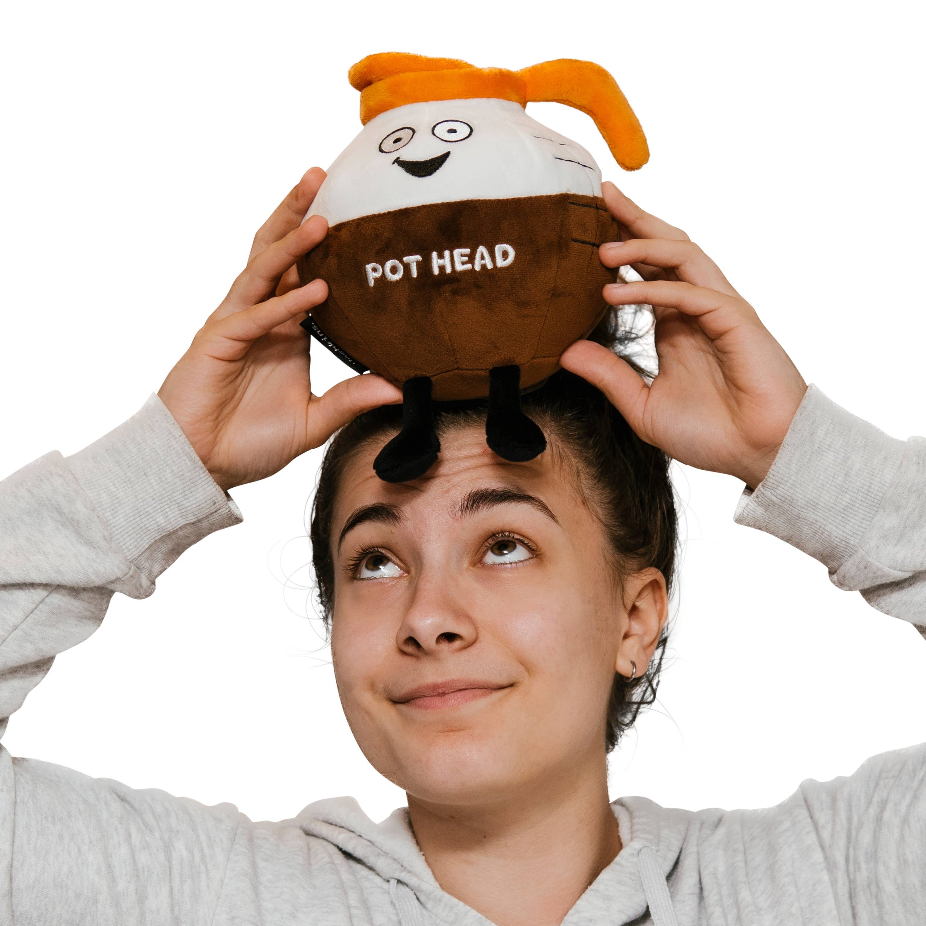 A brown and white coffee pot plushie with an orange pour spout. The white portion has a smiley face, and the brown portion features white text that says "Pot Head." The plushie has black legs sticking out.
