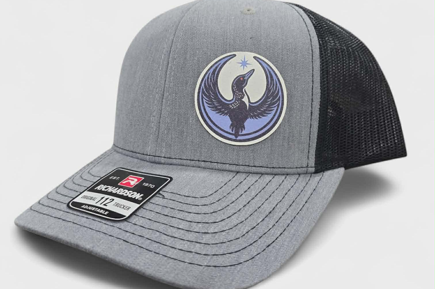 Gray and black trucker hat with a logo of a rebel loon on a light gray background