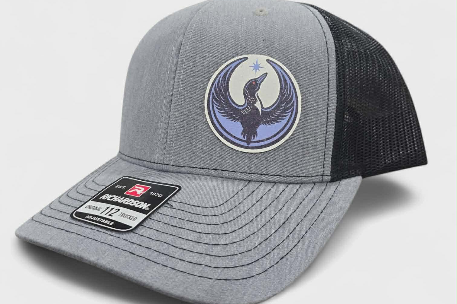 Gray and black trucker hat with a logo of a rebel loon on a light gray background