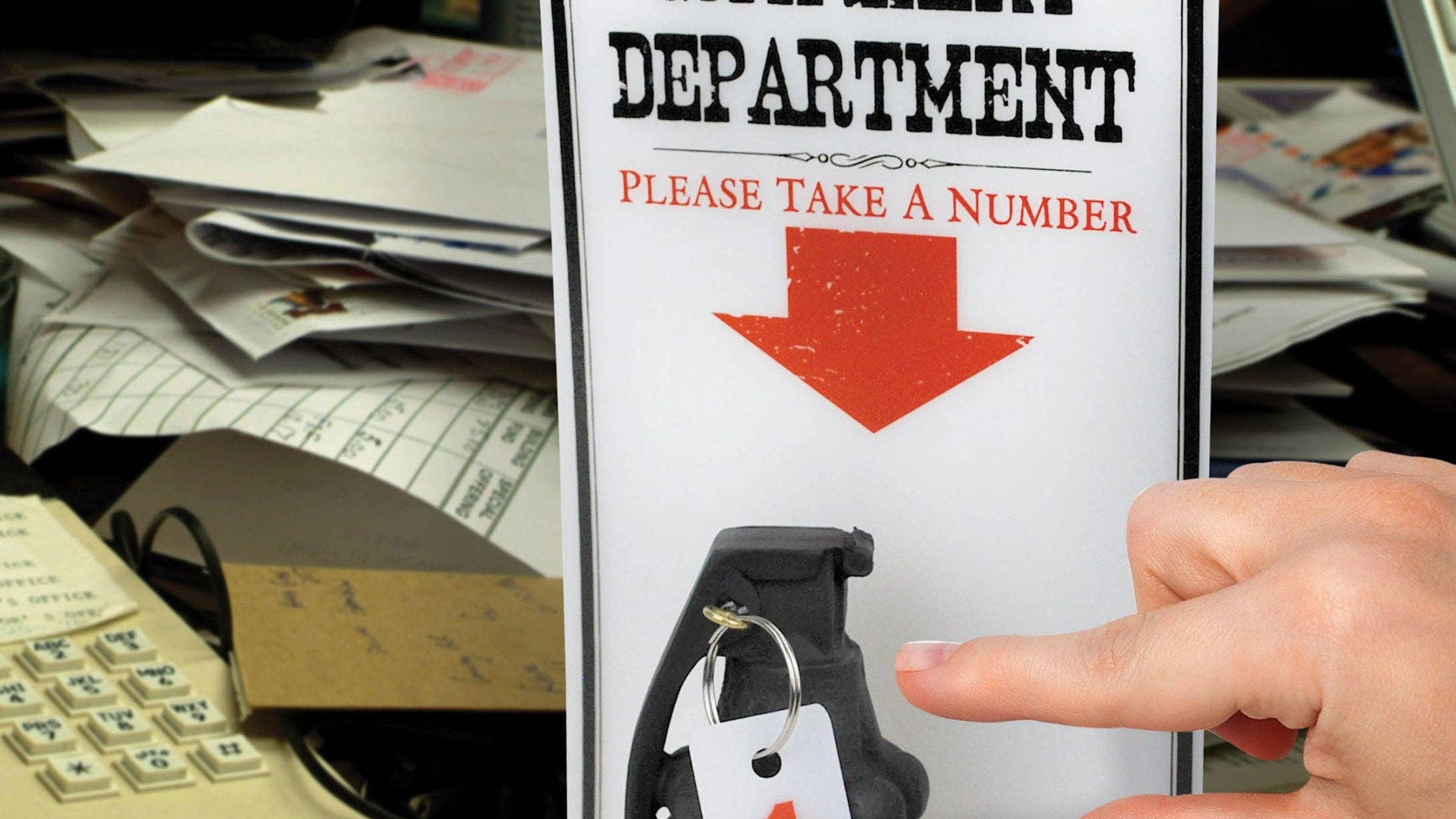 A hand reaches for a number tag attached to a grenade beneath a sign reading "Complaint Department, Please Take a Number," set on a cluttered desk.