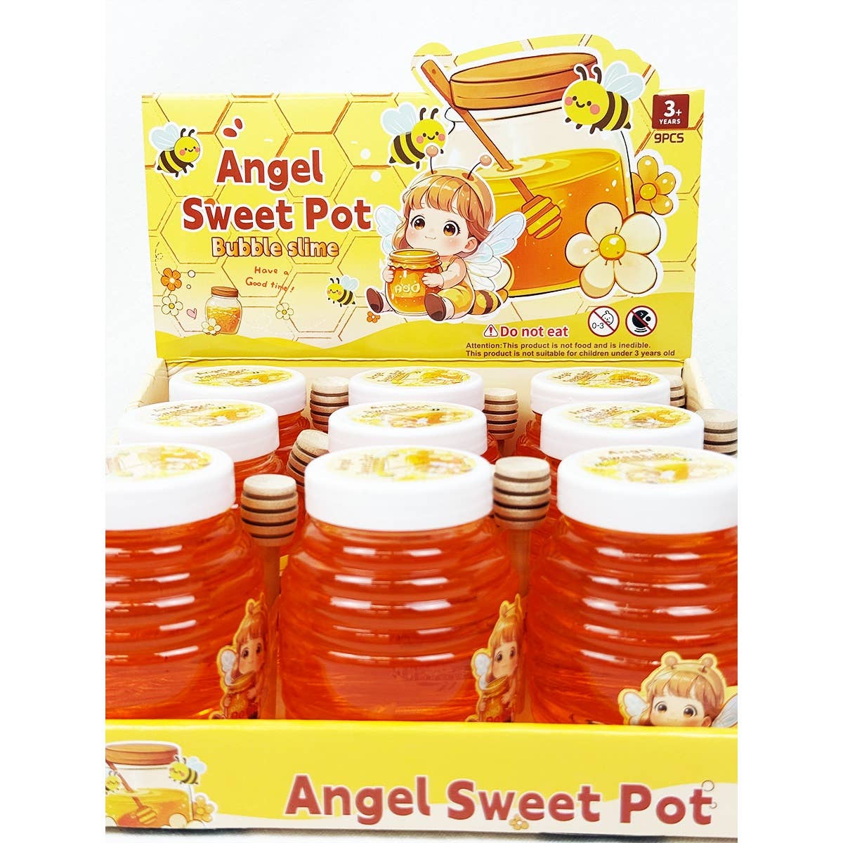 Display box of Angel Sweet Pot bubble slime jars designed to look like honey pots, with bright orange slime, white lids, wooden honey dipper accents, and bee-themed packaging featuring a cartoon child and bees.
