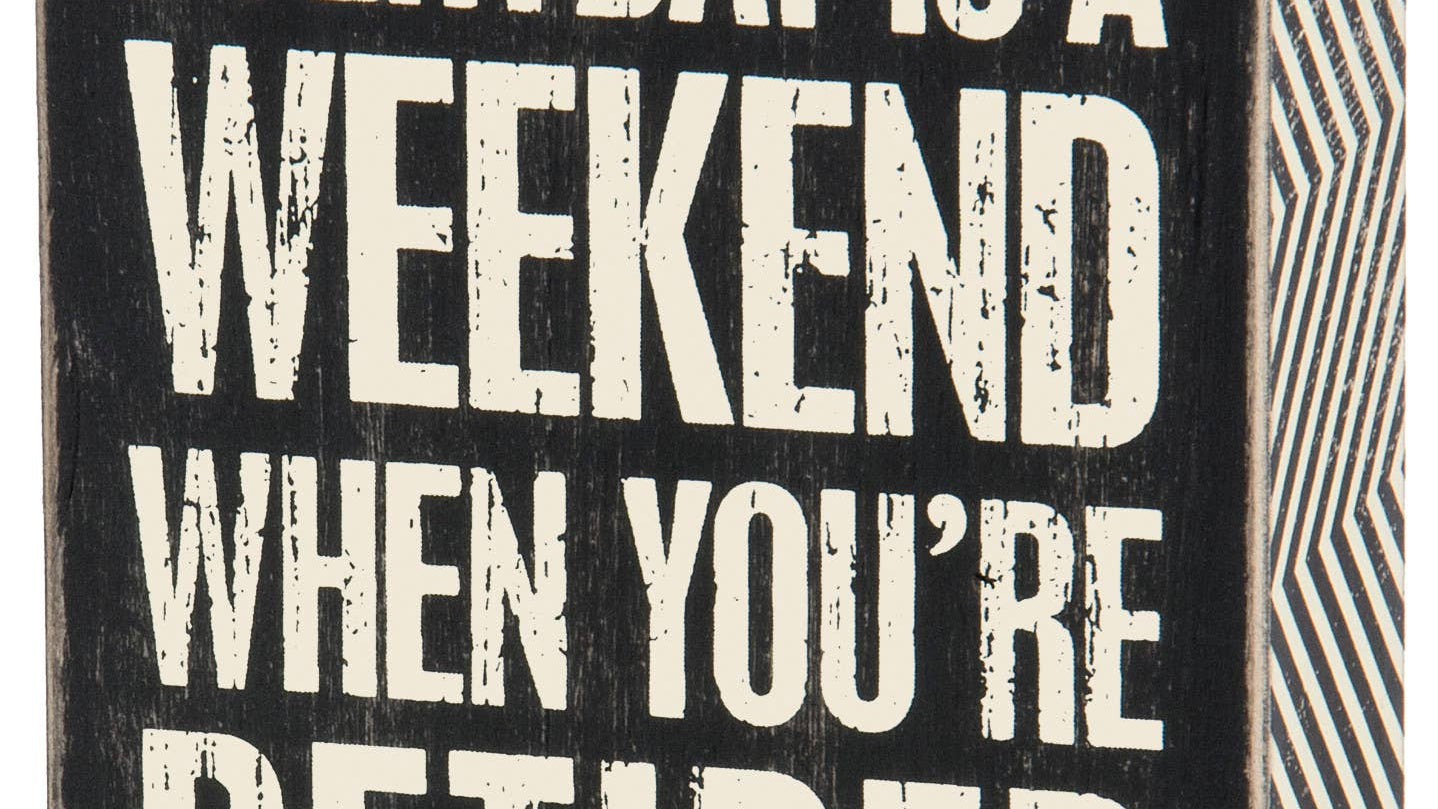 A square black wooden box sign with white capitalized text that reads 'EVERYDAY IS A WEEKEND WHEN YOU’RE RETIRED.' The sign features a distressed vintage finish and a decorative black and white zigzag pattern on the side panels.