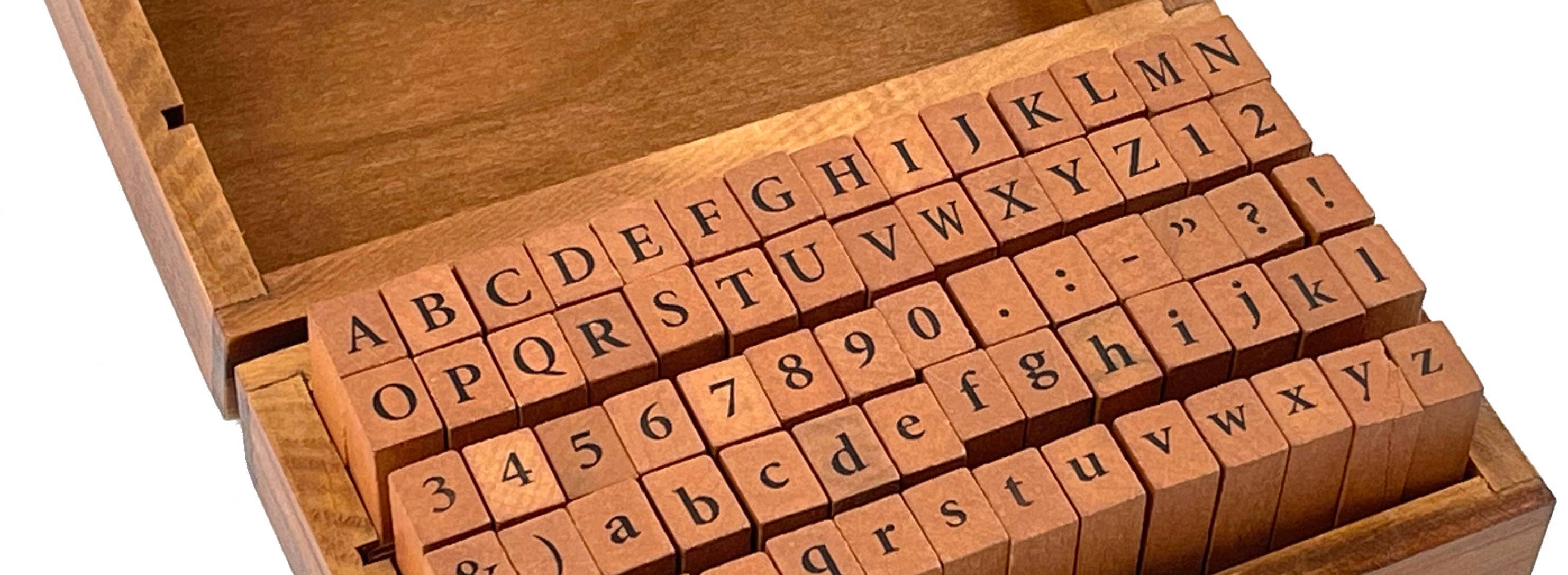 A wooden box with an open lid displays alphabet and number rubber stamps. The orderly arrangement conveys a sense of organization and creativity.