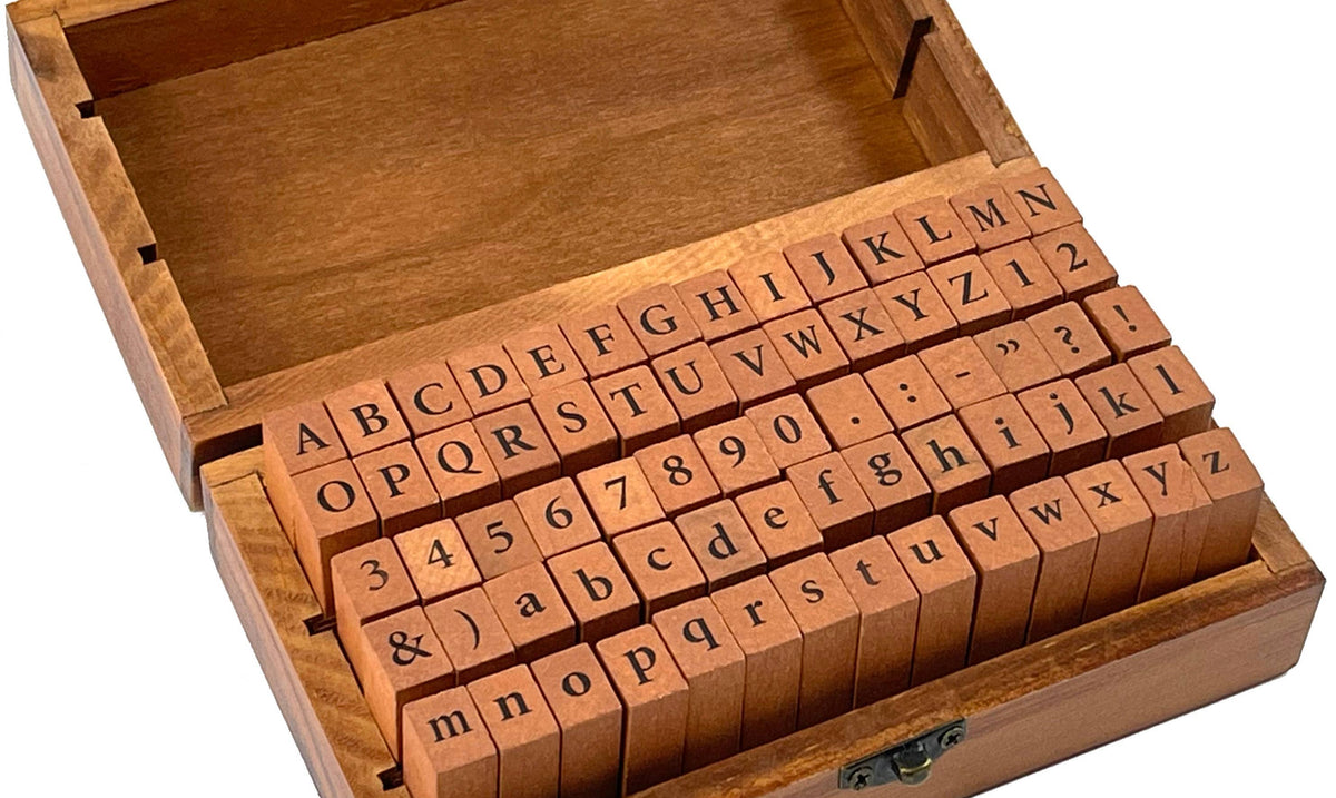 A wooden box with an open lid displays alphabet and number rubber stamps. The orderly arrangement conveys a sense of organization and creativity.